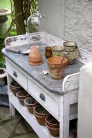 Zinc covered garden work bench with  ceramic and terracotta pots, trowel, bulbs and a glass cloche