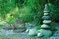 Sculptural tower of large pebbles with wooden panels inset in to a pebble path in a seaside style garden with grasses and bamboos - Designed by Alan Titchmarsh at Barleywood, Hampshire