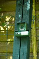 Sonic device for scaring off cats, fixed to wooden upright against fence