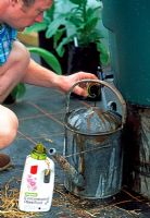 Man adding liquid plant feed to water in watering can