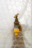 Vintage brass garden tap with a plastic adaptor insulated against frost with a sheet of bubblewrap and an old towel