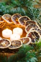 Festive arrangement of candles in wreath of dried orange slices and greenery