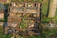 Stacked wooden pallets packed with stones, logs and bricks to provide dark nooks and crannies in which insects such as ladybirds, lacewings and bees can overwinter in a wildlife garden - The Eco Garden, Trentham Gardens, Staffordshire 