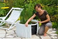 Woman attaching wooden cladding to mini pond to hide plastic container