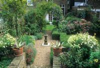 Small town back garden with gravel path, sundial, Clematis arch, lawn and low Buxus hedges