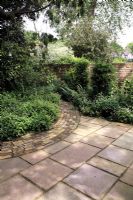 Mixed paving of Indian sandstone and brick in dappled shade, groundcover of Geranium oxonianum and Sylvaticum in borders, Aucuba, buxus, Taxus surrounding

