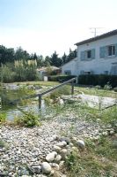 Natural swimming pond in South of France garden edged with large pebbles Pampas grass and house in background