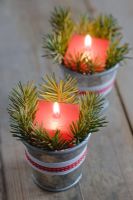 Red candles in mini zinc buckets with fir tree foliage and ribbon as a table decoration.