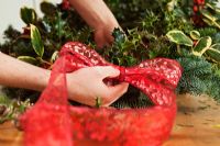 Making a Christmas wreath - Attaching red ribbon to holly wreath
