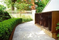 Corten steel is used throughout this London garden. Here it boarders the paths, and creates a storage area for the rubbish bins, further disgused by a chain-link curtain.