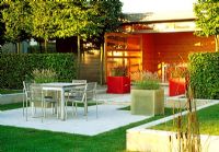 The garden room opens onto the dinning terrace, semi-screened by pleached hornbeam and hedging, in this Belgium garden. Red and white fibreglass, cube planters with pennisetum and Imperata cylindrica.