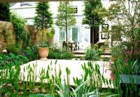 From this pale green, furnished garden apartment, sliding doors open onto an interior courtyard. The space is divided by pleached hornbeams and boarders of delicate perennials and including a stip shaped pond.