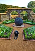 'Dark Planet' pebbled sculpture and dog in formal walled private garden