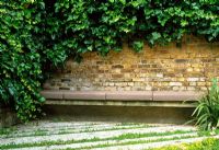 A seating area at the rear of the garden. Ivy greens the wall, alternating strips of textured concrete and sedum create the floor