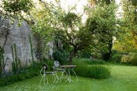 Spring garden with table and chairs underneath apple trees 