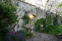 Walled garden with apple blossom and early morning sun shining through a gateway