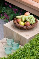 Basket of fruit and plastic tumblers on a square block table. Eco Chic Garden, sponsored by Helios - Gold medal winner for Best Urban Garden at RHS Chelsea Flower Show 2009