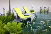A glass seating area above fast flowing water surrounded by planting of Ferns, Iris sibirica and Astrantia in The Witan Wisdom Garden, sponsored by Witan Investment Trust - Silver Flora medal winner for Urban Garden at RHS Chelsea Flower Show 2009