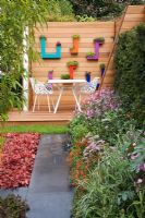 Raised deck in bold modern urban garden with Heuchera 'Peach Flambe' and a colourful herbaceous border edging slate pathway - The PSI Nursery Garden, sponsored by PSI Nursery - Silver Flora medal winner for Urban Garden at RHS Chelsea Flower Show 2009  