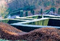 View over the Yew hedging from within the 'Grasses Parterre'. Beech 'wavy' hedge in foreground. Part of the 'wild garden' and view to wood beyond hedges - Veddw House Garden in February