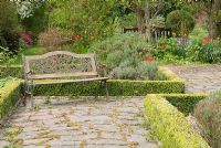 Decorative metal and wooden bench in the formal Rose garden, with Buxus hedging and paths of Westmorland slate - Poulton Hall, NGS garden, Cheshire