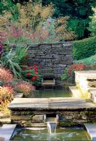 The formal pools and view to the vegetable garden with Stipa gigantea and Persicana 'Fire Tail' on other side of the wall and Acaena Microphylla 'Kupferteppich' at pool edge - Lower House, Cusop, Near Hay-On-Wye