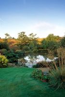 Overview of lake with Stipa gigantea and Bergenia by path - Lady Farm, Chelwood, Somerset