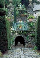 Statues of reclining lion in arch with blue and gold painted railing above and view to cottage outside the garden - Plas Brondanw