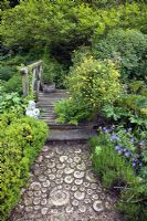 Shell designed path leading to wooden footbridge over landscaped water garden - Millennium Garden NGS, Lichfield, Staffordshire