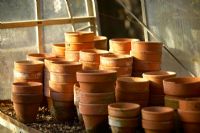 Terracotta pots in old glass gardening shed in soft autumn evening
