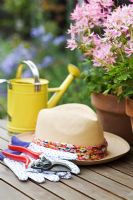 Sunhat, gloves and secateurs on garden table with pink Pelargonium