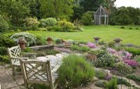 Overall view of alpine garden planted with many aromatic alpines with wooden chairs looking out onto lawns with borders of herbaceous perennials and beautiful green oak gazebo - Woodpeckers, Warwickshire