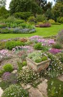 Scree Garden leading to lawn with borders of herbaceous perennials and mature trees - Woodpeckers, Warwickshire