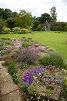 Garden view of alpine garden planted with many aromatic alpines planted in gravel old stone troughs looking out onto lawns and borders of herbaceous perennials - Woodpeckers, Warwickshire
