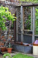 Rustic lean-to or greenhouse with tinbath water butt and rusty metal fish tail focal point
