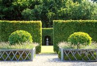 Geometry formalises a space. Tall beech linear hedges enclose a large space while outside decorative low wooden railings enclose box, lavender and green spheres 