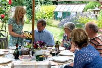 Family group enjoying summertime alfresco dining with woman serving potatoes 'Maris Bard' freshly harvested from the garden