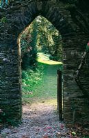 Caerhays Castle Gardens, St Austell, Cornwall. View through archway in wall that runs up the hill from the castle. Primorses in grass beyond.