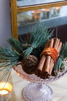 Christmas decoration of bundles of scots pine and cinnamon with orange ribbon in glass dish