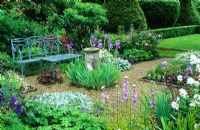 Formal garden with blue painted wrought iron bench, old sundial, gravel paths, roses and planting of Campanula latiloba 'Hidcote Amethyst', Stachys byzantina, bearded irises, Astrantia 'Hadspen Blood' and view to lawns with box hedging and Yew topiary -  Cerne Abbas, Dorset
