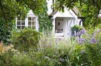 Borders of herbaceous perennials in front of black and white barn door with flowers in profusion, packed into an idyllic English cottage garden, at Grafton Cottage , NGS, Barton-under-Needwood Staffordshire 