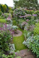 Colour themed borders of herbaceous perennials brick circle with well planted container wooden seat in The Dell with flowers in profusion, packed into an idyllic English cottage garden, at Grafton Cottage ,NGS 