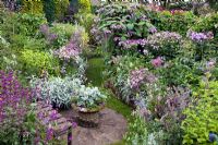 Colour themed borders of herbaceous perennials brick circle with well planted container wooden seat in The Dell with flowers in profusion, packed into an idyllic English cottage garden, at Grafton Cottage , NGS 