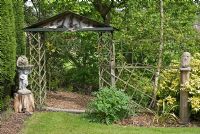 Decorative sculptures with trellis and archway, leading to bark chipping path adjacent to hedge at Aureol House, NGS garden Lancashire