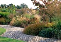 Curved cobbled path lines this grass border with Molinia caerulea 'Transparent' 