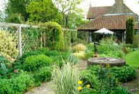 A pergola runs the length of the garden screening the entrance from the front garden, perennials. An old well becomes a focus point.