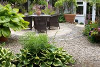 Rattan chairs and table on circular stone and gravel patio - Montford Cottage, NGS garden, Lancashire