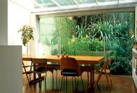 Glass wall and roof give light to this basement dining area opening onto a compact subtropical garden in London. Astelia chathamica, Equisetum fluviatile, water horsetail , Hedychium gardnerianum, Ginger and ferns. 