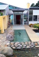 Styalised nature including fish swimming in a river complete the front entrance to this art collectors home. Tropical cycads, textures of stones and boulders. Waiheke, New Zealand