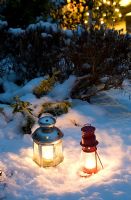 Tea light lanterns in snow backed by foliage and Christmas tree